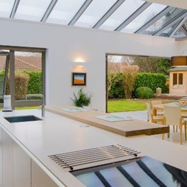A kitchen with a glass ceiling and large bifold doors leading out into the garden