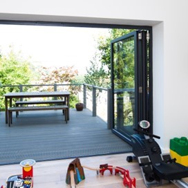 A bright room looking out through fully opened folding doors onto an upper storey decking area