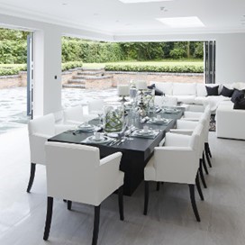A bright dining area looking with a large folding door and corner door section fully open looking out onto a paved area