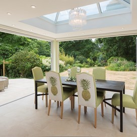 Set of green chairs around a dining table facing the garden through a open white bifold door
