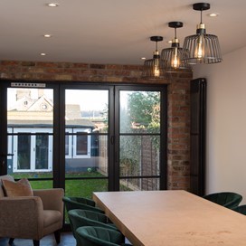 Large dining table surrounded by chairs next to closed bifold doors looking out towards the garden