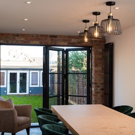 Large dining table surrounded by chairs next to half open bifold doors looking out towards the garden