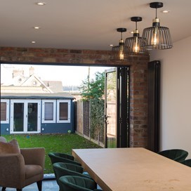 Large dining table surrounded by chairs next to open bifold doors looking out towards the garden