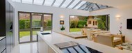 A kitchen with a glass ceiling and large bifold doors leading out into the garden