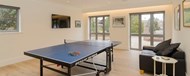 A games room with a table-tennis table, large wall-mounted TV, a leather sofa and two sets of folding doors