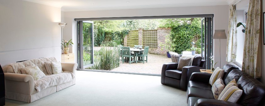 The view from a lounge looking through open bifolding doors, which cover a whole wall, into the garden