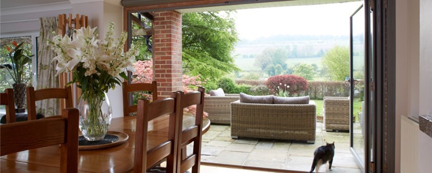 Looking over a dining table, through open patio doors and out into a paved area with wicker sofas