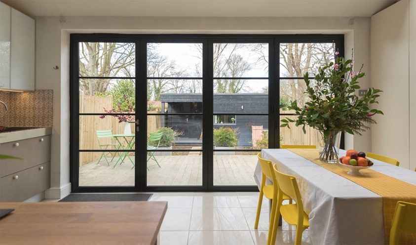 A set of closed bifold doors overlooking a modern homes garden with the view of a garden home in the background