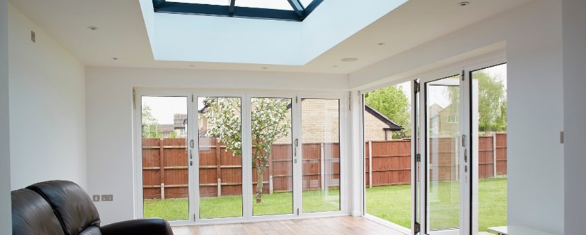 A garden room with wooden floors, a large skylight and large floor to ceiling glass doors across two walls