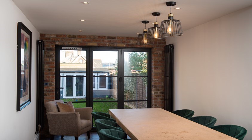 Large dining table surrounded by chairs next to closed bifold doors looking out towards the garden