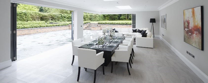 A bright dining area looking with a large folding door and corner door section fully open looking out onto a paved area