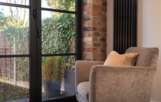 Cream chair in the corner of the room looking out through bifold doors to a garden